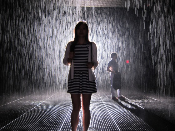 Two women standing within the MoMa's large scale installation, the Rain Room, created by Random International. Don't worry about your hair, ladies, this downpour rain won't get you wet!