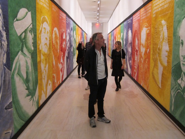 Observers of Mike Kelley's Retrospective at MoMa PS1 walking down the part of the exhibition entitled "Hall of Shame", which is a colorful hallway of portraits of famous people