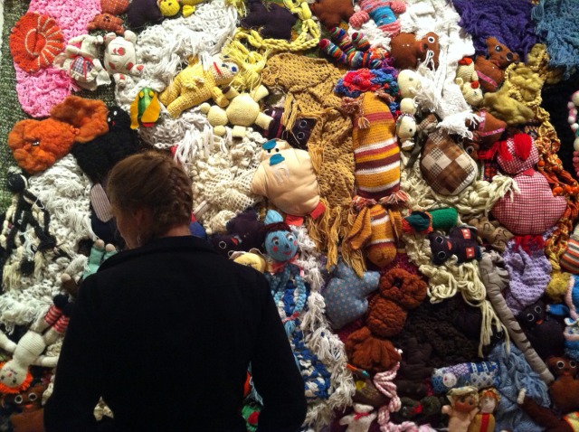 Man admiring Mike Kelley's MoMa PS1 exhibition with a large variety of stuffed animals sewn together into a big piece that covers the wall.
