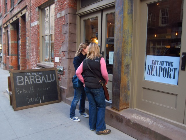 Two women read the menu outside of Barbalu restaurant on South Street Seaport next to a sign that reads "One year later, Barbalu rebuilt after Sandy"