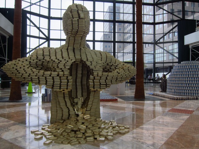 Man made out of cans that is reaching in and opening up his chest on display at the Canstruction exhibition, entitled "Pour Your Heart Out" by Leslie E. Roberts Associates
