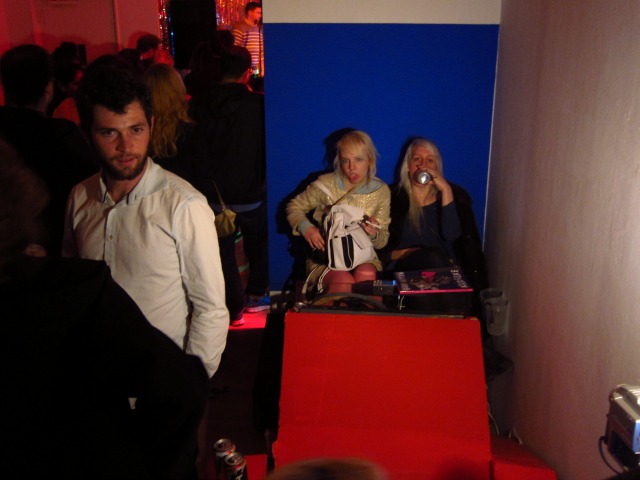 Two girls sitting down at the drinking beers waiting for their turn to get up at sing karaoke