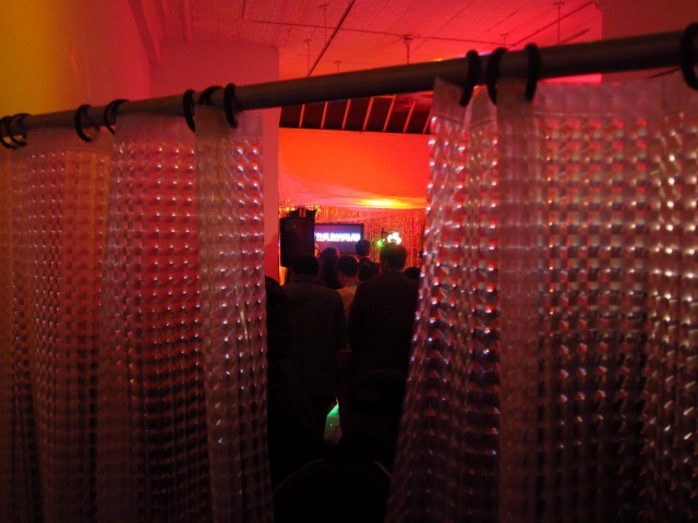 Peeping through the shower curtain hanging at Apexart's Scaryoke with a crowd of people behind watching someone sing karaoke