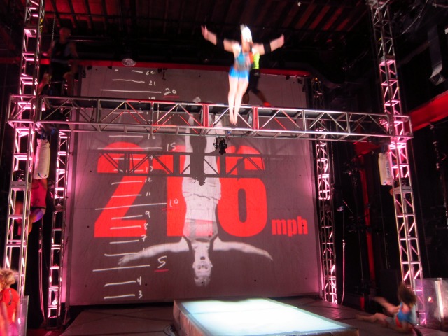 STREB Company crew member in action as she dives off the metal stage beam arms stretched out