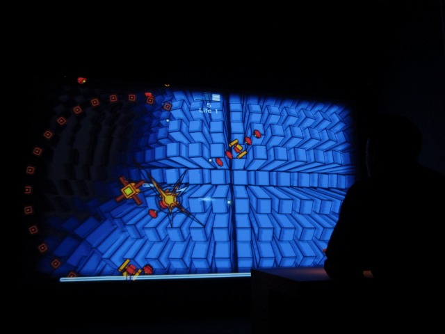 Close up image of the screen where someone is playing a shooter video game with yellow spaceships and a blue background