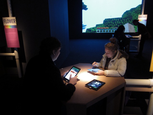 Image of Museum of Moving Image exhibition visitors playing video games on tablets at a wooden table