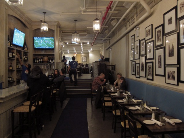 Image of the interior of Kefi's restaurant, showing some seating and people sitting at the bar watching football on the TV's