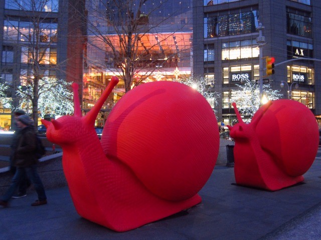 Two big red snails in front of the lit up Christmas lights and NYC buildings 