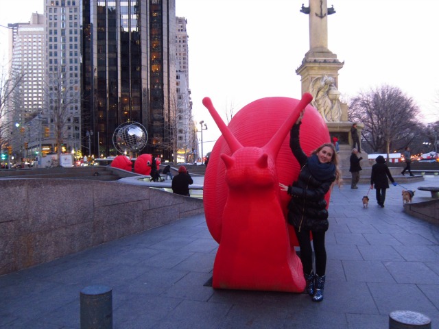 Outside of Trump tower a young girl poses next to one of the red snails popping up all over NYC