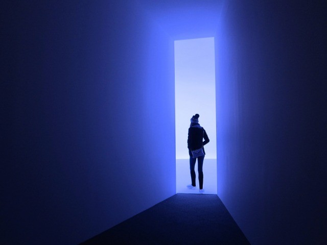 Young women turns the corner of a doorway lit with blue light at Doug Wheeler's installation at David Zwirner Gallery