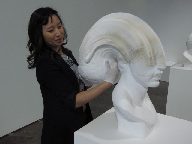 Chelsea art gallery assistant twisting back Li Hongbo's bust sculpture to show the layers of soft paper that its made out of