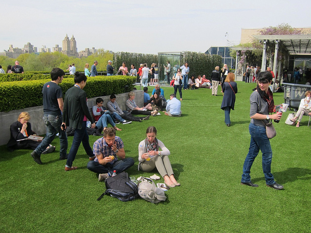 Dan Graham's Met Roof Garden pavilion covered in people lounging, walking around, and enjoying the installation