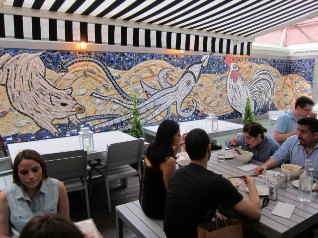 Customers sitting in the Ivan Ramen garden seating area, with a large mosaic tiled wall and a black and white striped roof 