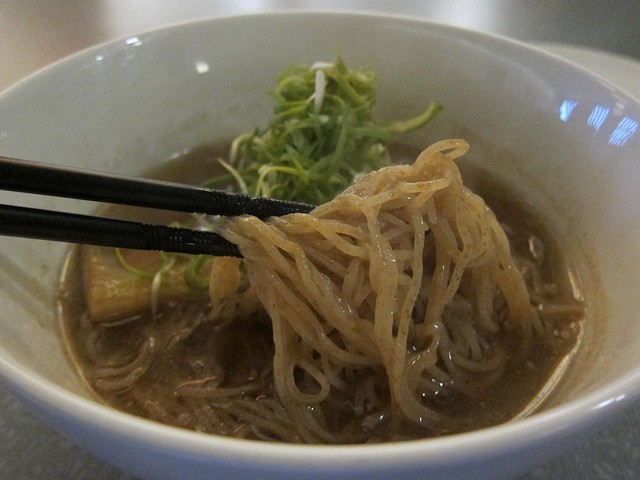 A pair of chop sticks digging into the ramen at Ivan Ramen made with rye noodle, sea salt, chicken-based broth, and tender pork chashu
