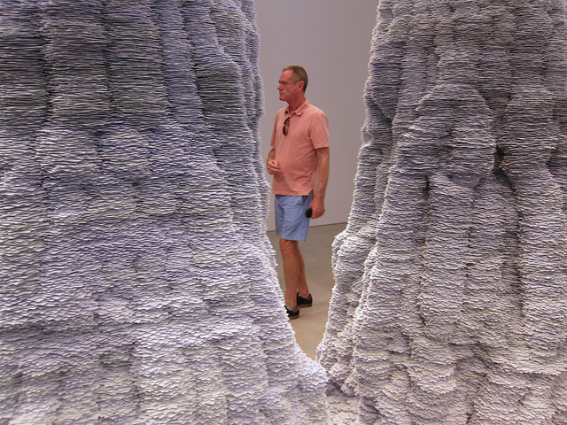 A man walking between two of Tara Donovan's index card sculptures.