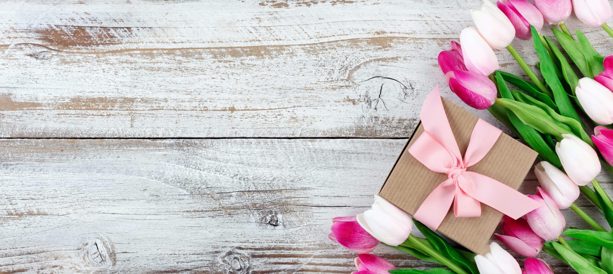Tulips and a box gift wrapped with pink ribbon on wood