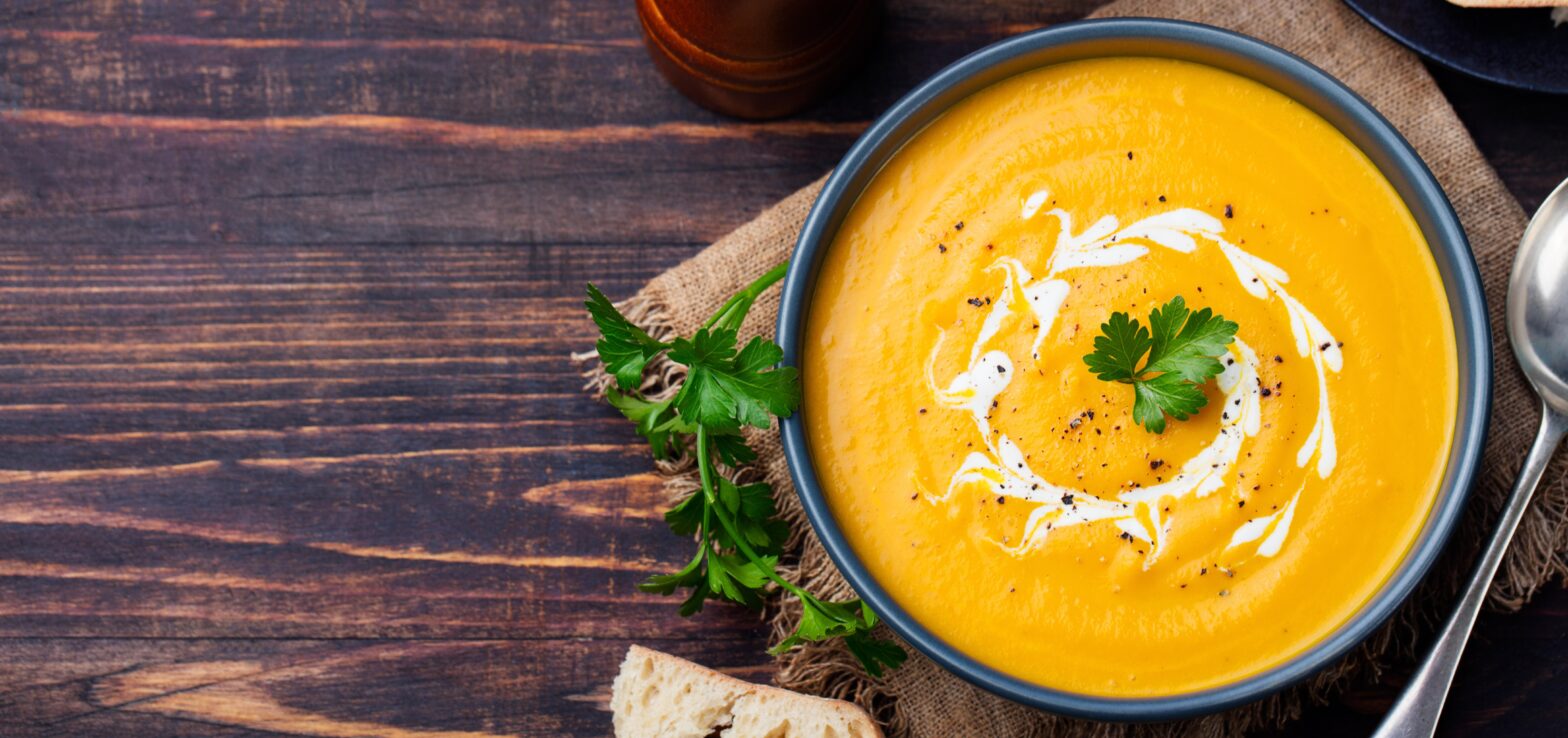 Pumpkin and carrot soup with cream and parsley on dark wooden background Top view Copy space.